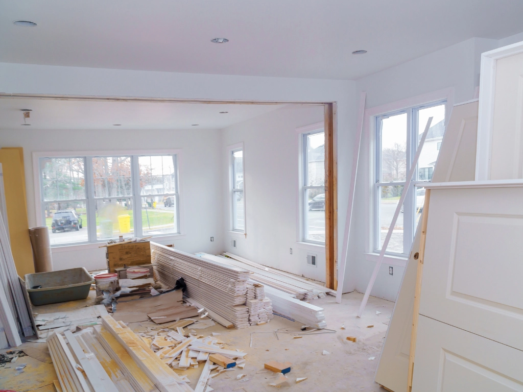 Interior home renovation in progress with stacked drywall, trim materials, tools, and construction debris