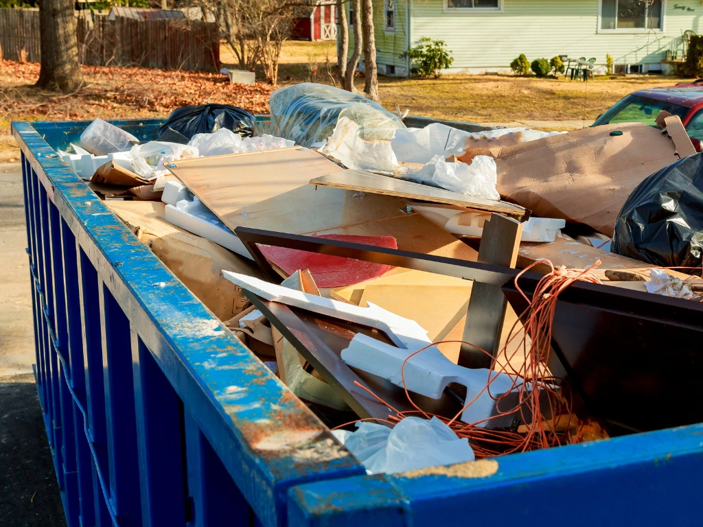 Large blue dumpster filled with cardboard, trash bags, and construction debris